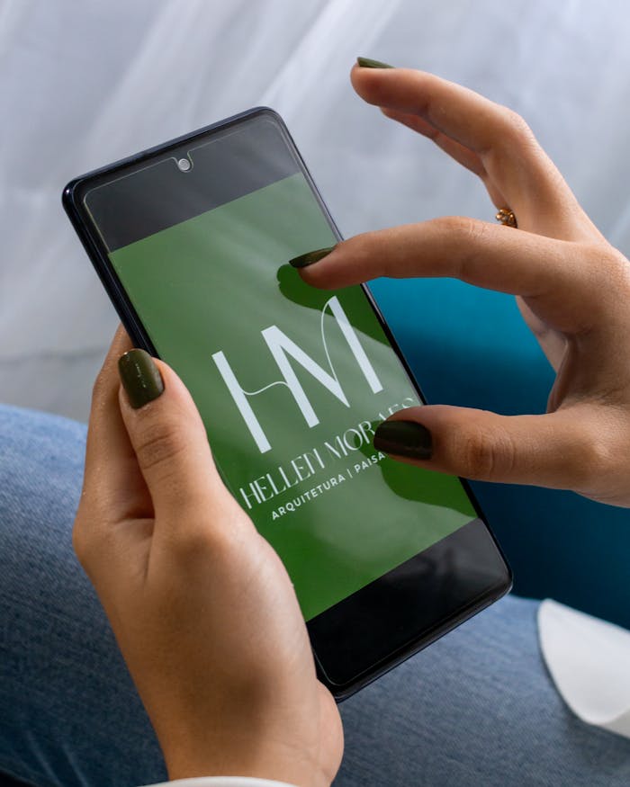 Female hands holding smartphone displaying Hellet Morais logo, close-up.